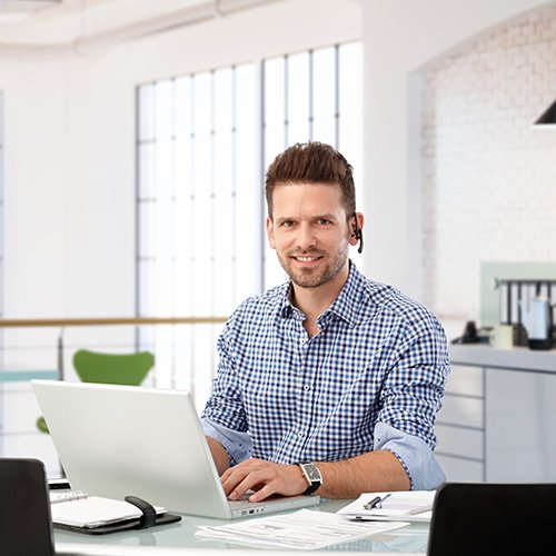 Ein Mann in einem Buero, der an einem Laptop arbeitet und ein Headset trägt