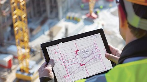 Fachkraft nutzt Tablet zur Planung und Kontrolle von Gebäudeautomation auf einer Baustelle